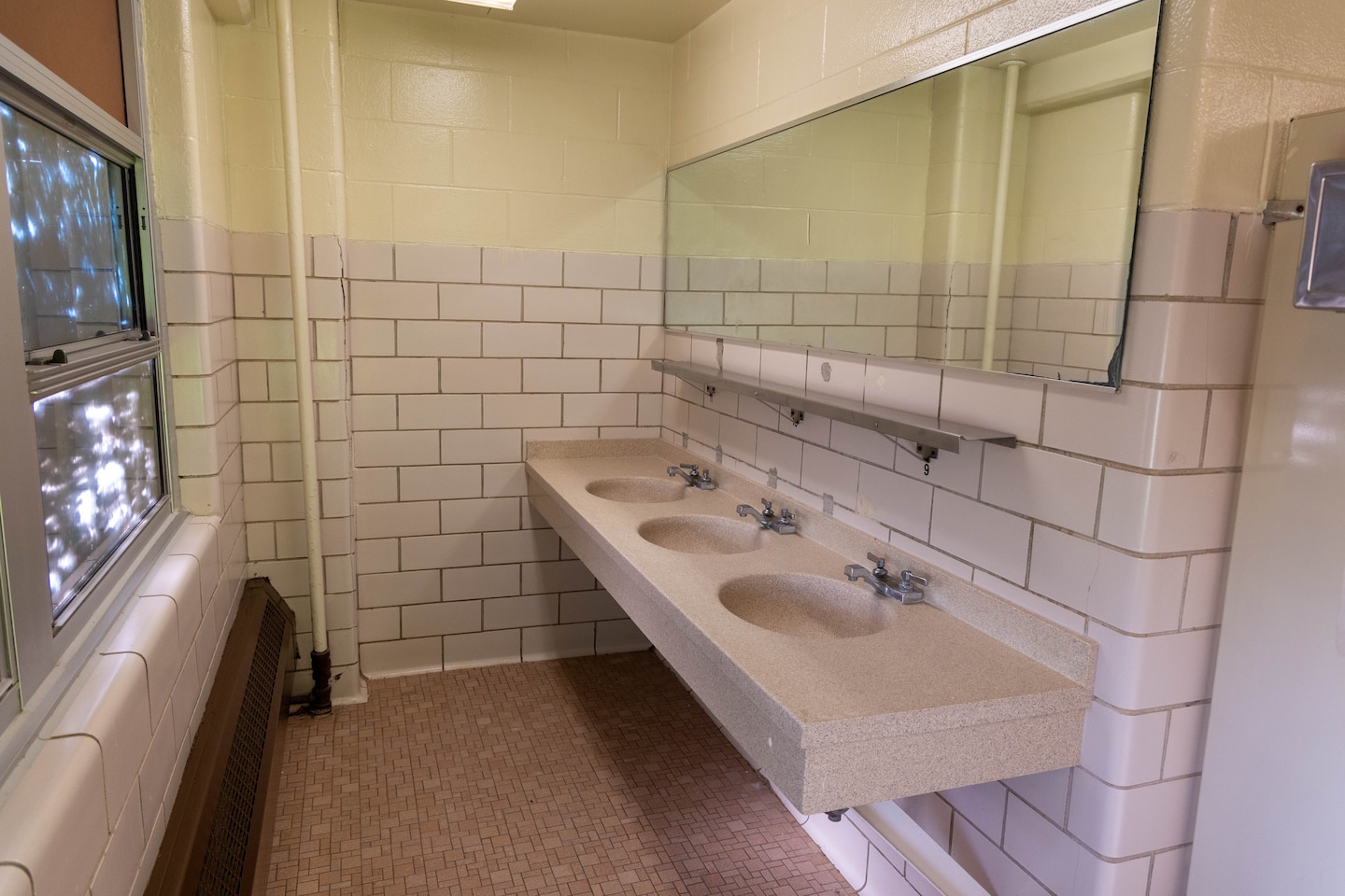 A bathroom with three sinks and a mirror with beige floors and tile walls.