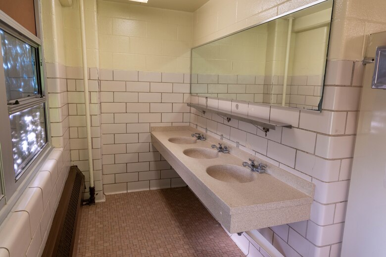 A bathroom with three sinks and a mirror with beige floors and tile walls.