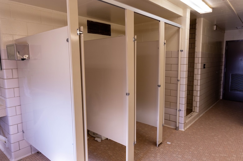 A bathroom with three stalls with beige floors and tile walls.
