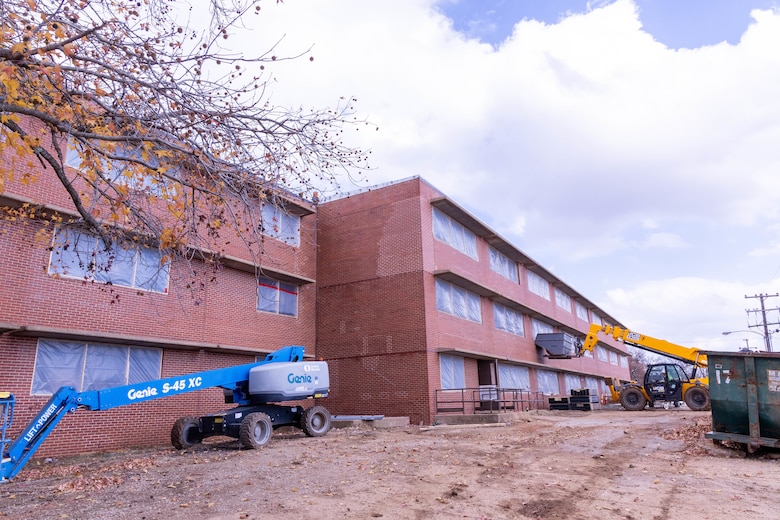 A three-story red brick building under construction with dirt in the foreground and a cloudy sky in the background.