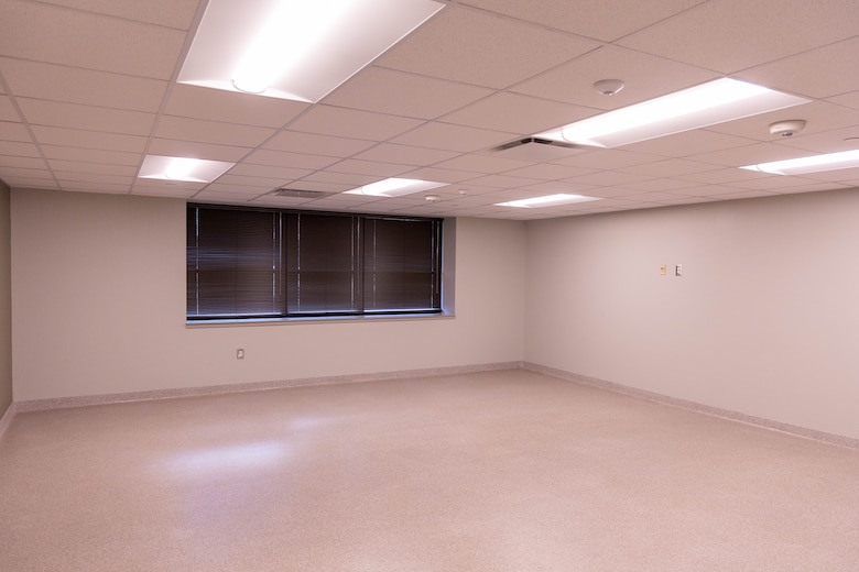 A beige room with a window and drop ceiling with lights.