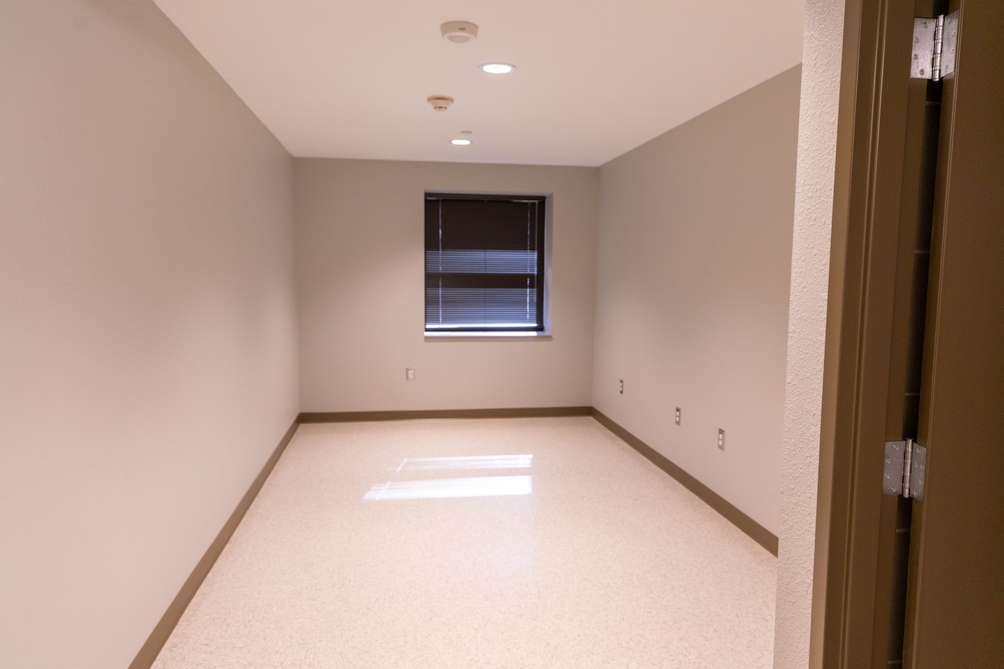 A beige room with a window and a brown door to the right.