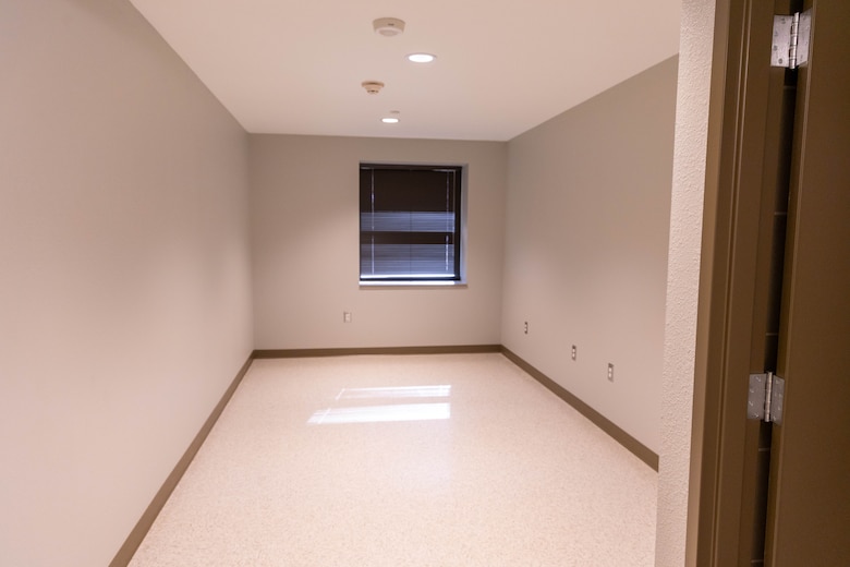 A beige room with a window and a brown door to the right.