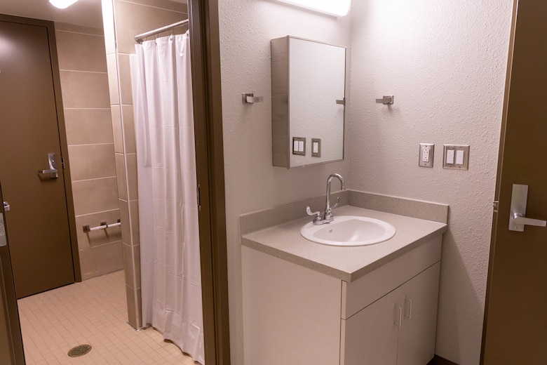 A bathroom with beige walls and tiles, a sink, mirror and brown door in the background.