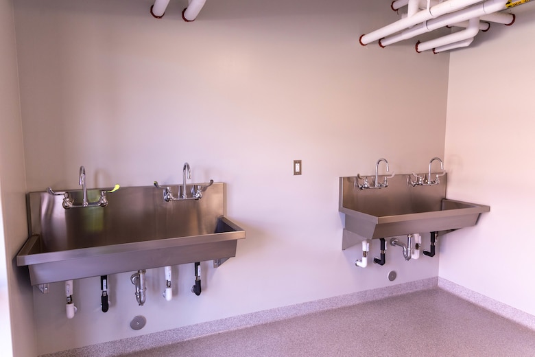 A beige room with grey floors and two silver sinks.