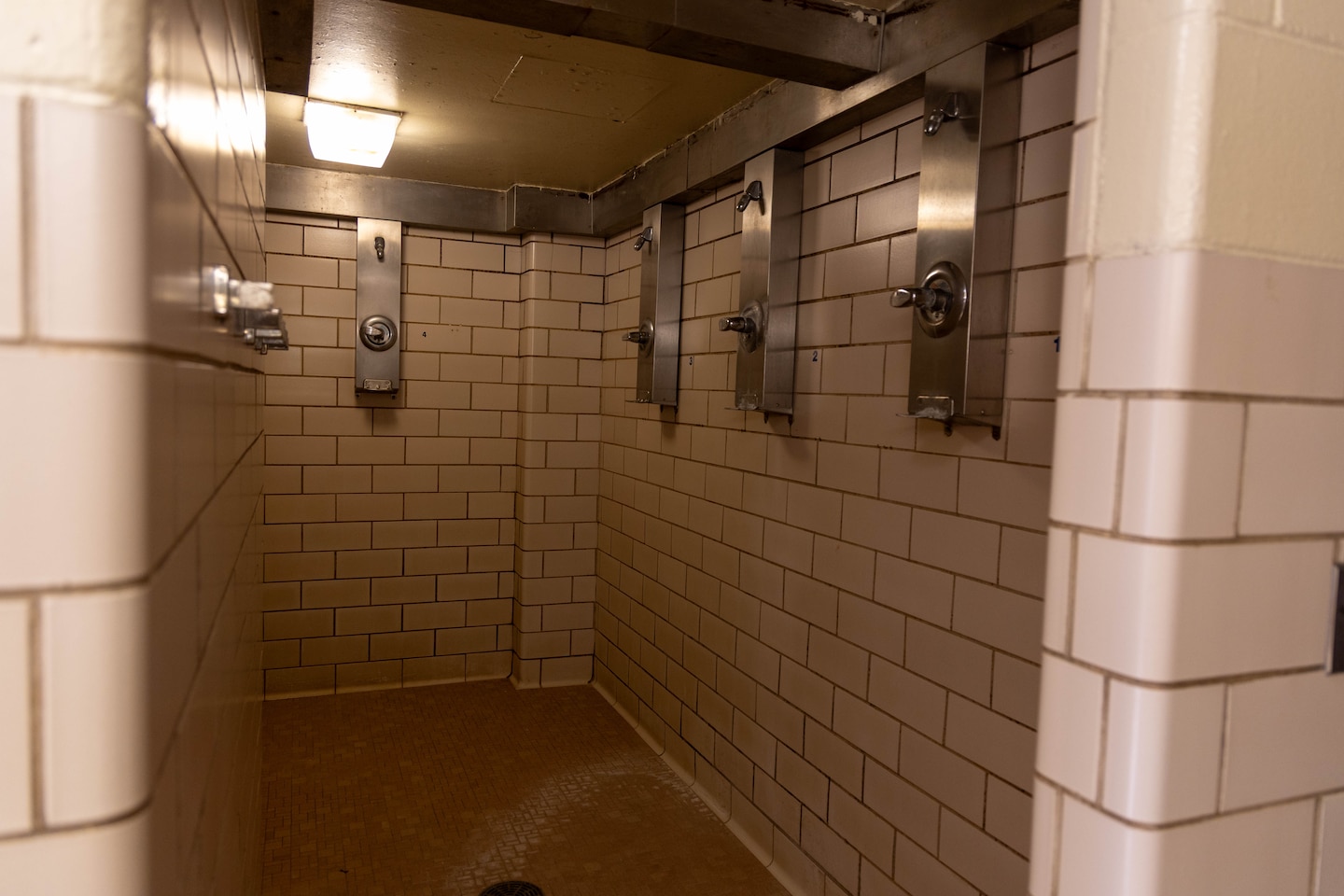 A communal shower with beige tiles and silver shower heads.