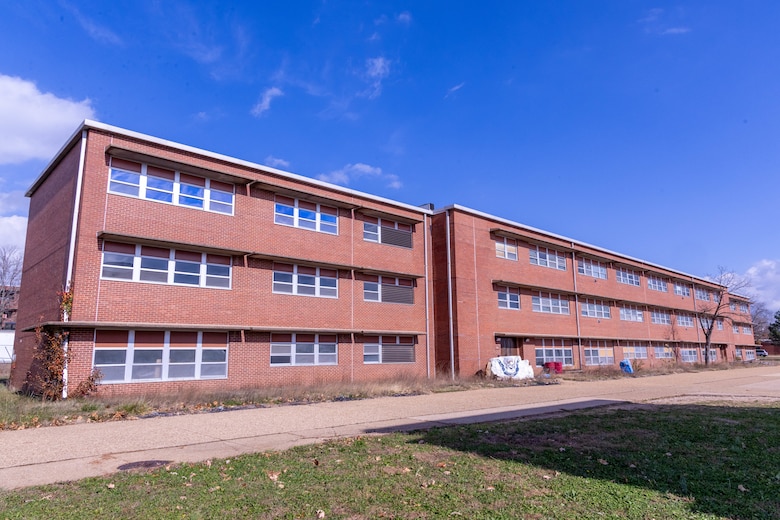 A red brick building with three stories and windows with green grass in the foreground and blue sky in the background.