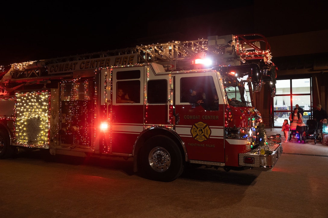 Firefighters with The Combat Center Fire Department, Marine Corps Air Ground Combat Center drive a fire engine in the Holiday Light Parade during the Holiday Festival at Freedom Plaza, Twentynine Palms, California, Dec. 2, 2025. The festival is an annual event that The Combat Center takes part in, featuring a parade, a tree lighting ceremony, and food vendors for the families of Twentynine Palms and MCAGCC. (U.S. Marine Corps photo by Lance Cpl. Jozef P. Majewski)