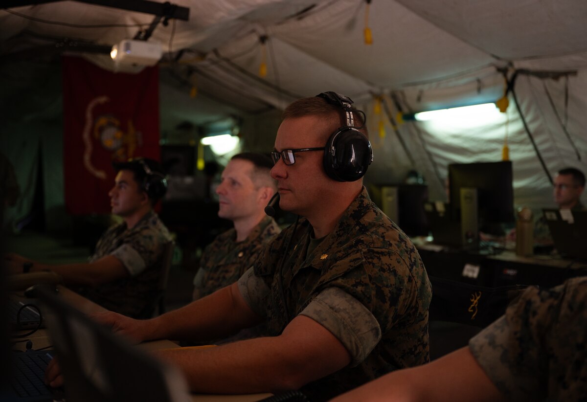 uniformed U.S. Marines wearing headsets work at computers in a tent