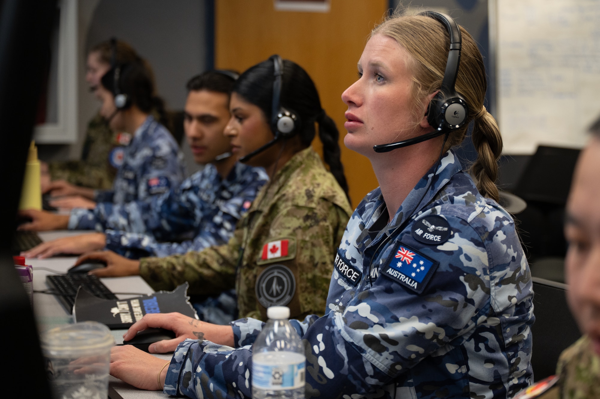uniformed RAAF and RCAF members wearing headsets work on computers