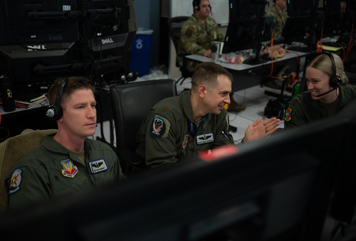 uniformed USAF and RCAF members wearing headsets work on computers