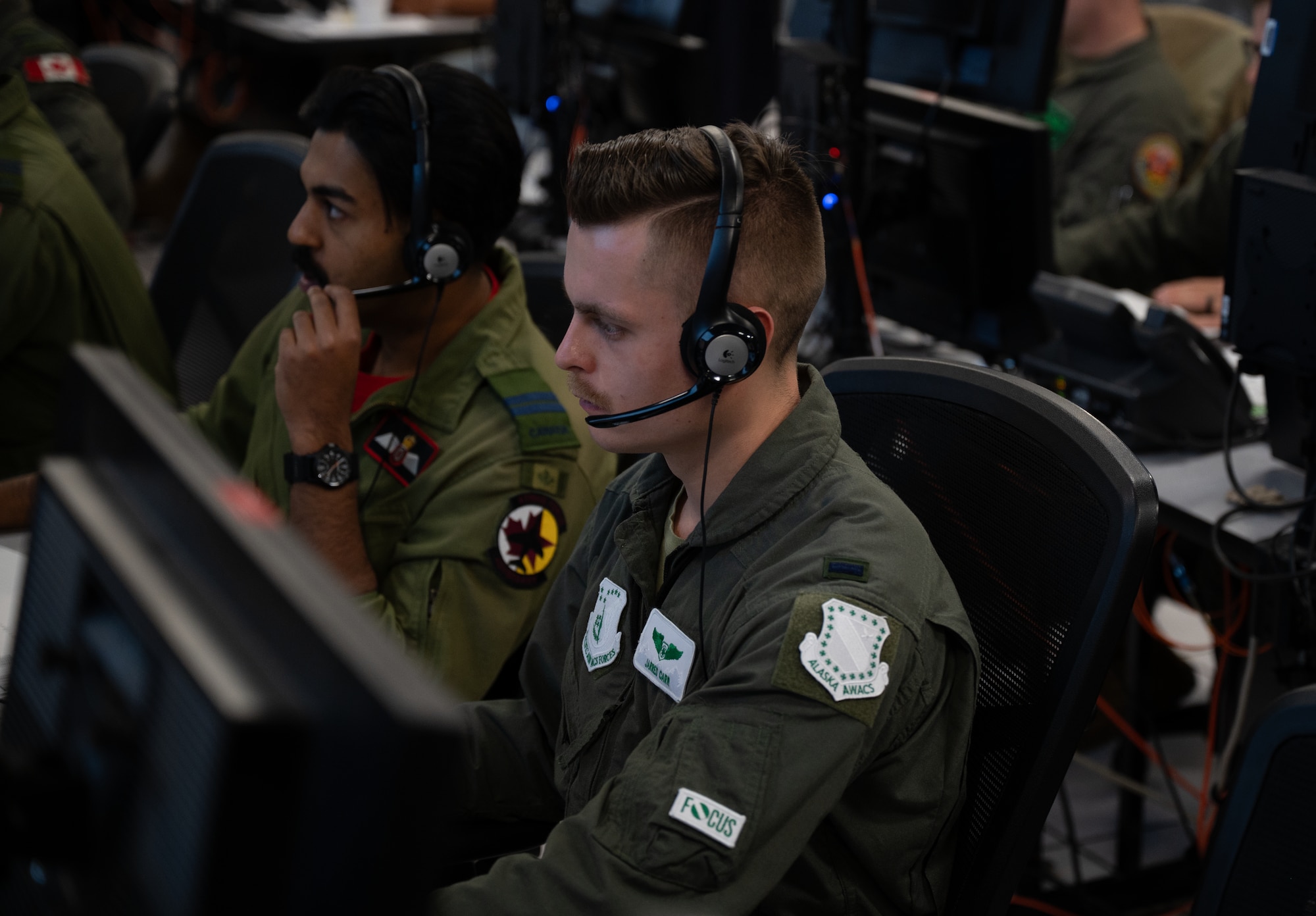 uniformed USAF and RCAF members wearing headsets work on computers