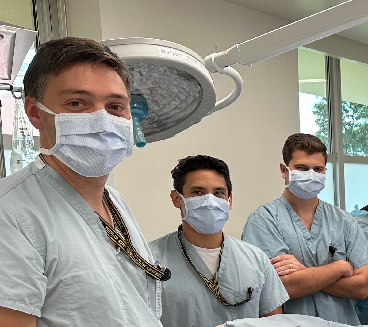 Three doctors wearing face masks pose for a photo in an operating room.