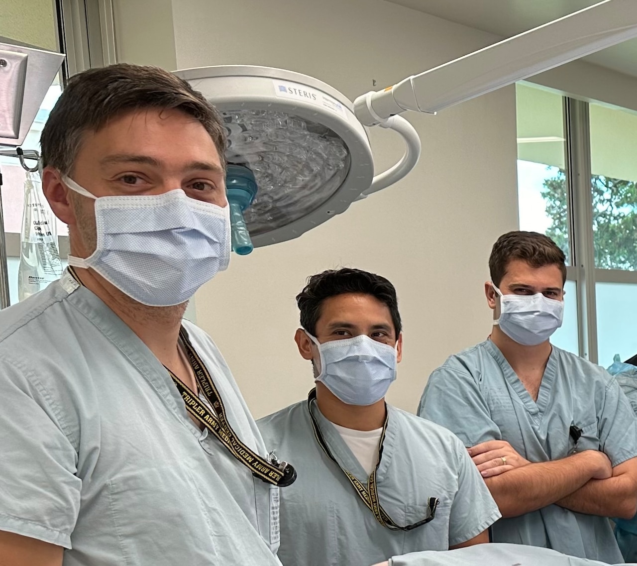 Three doctors wearing face masks pose for a photo in an operating room.