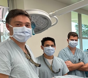 Three doctors wearing face masks pose for a photo in an operating room.