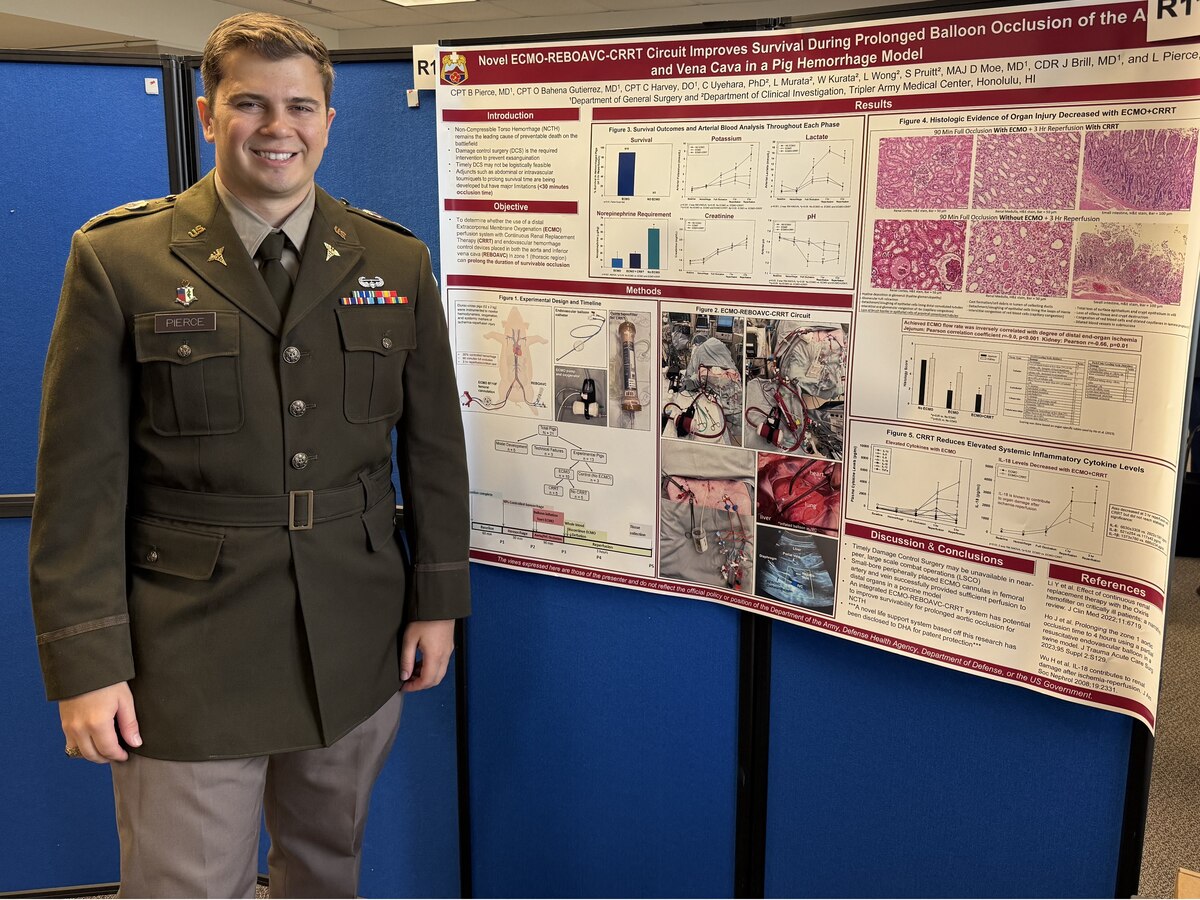 A man wearing an Army dress uniform smiles as he stands next to a display board.