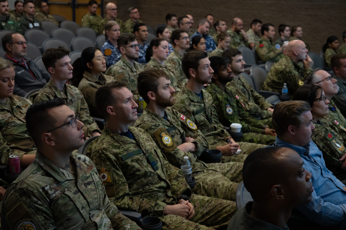 Coalition members sitting in stadium seating, listen to briefer.