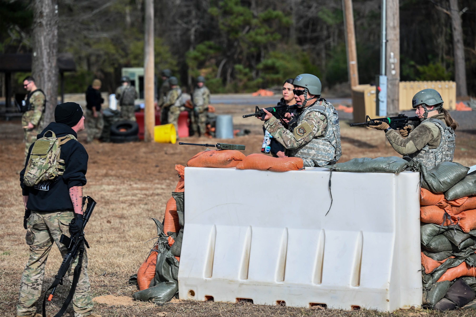 Airmen guard a defensive fighting position as a simulated opposing forces member approaches wearing a black hoodie.