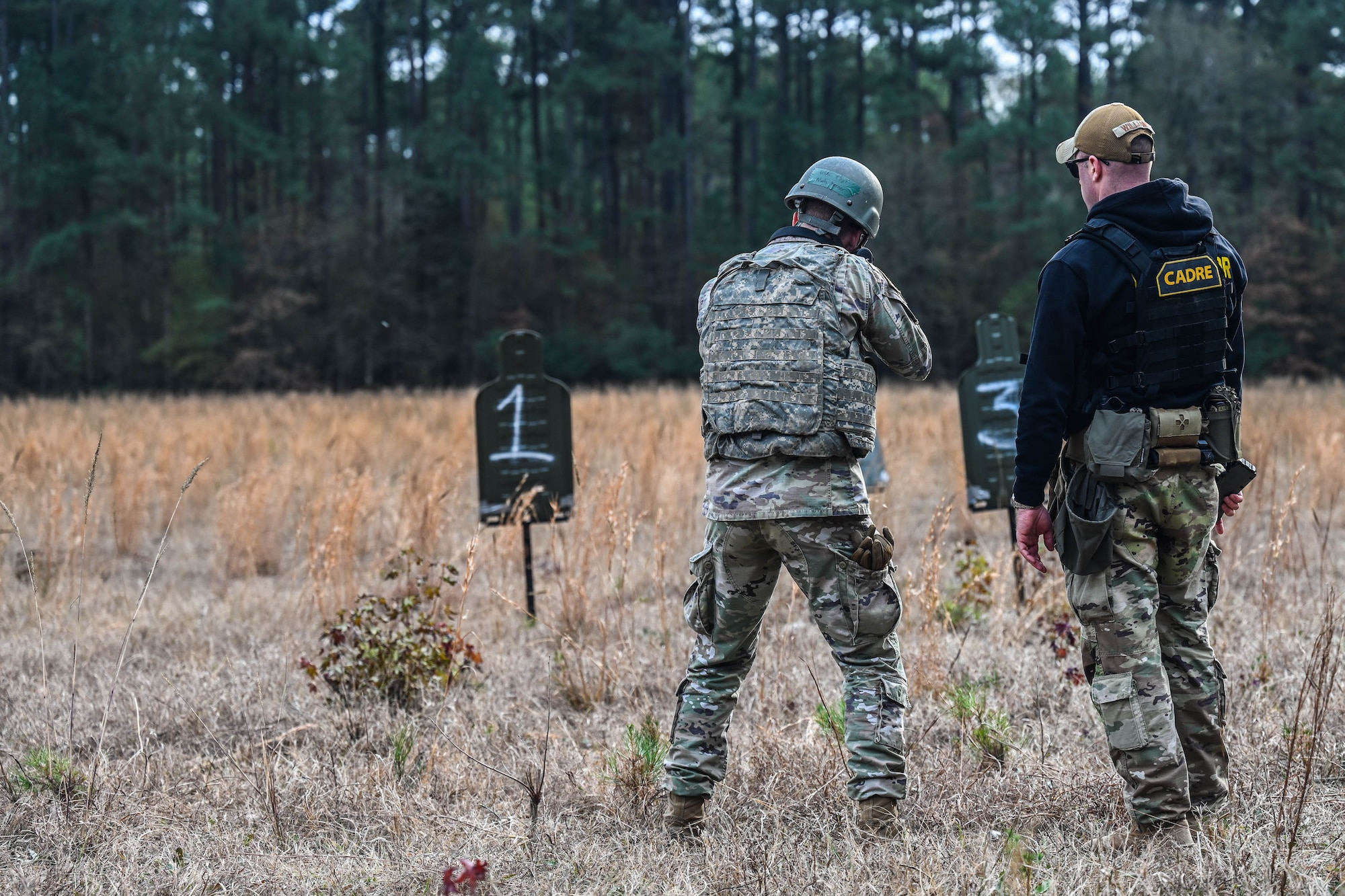 An instructor provides instruction to an Airman during a weapons training exercise with a target visible with the number one on it.
