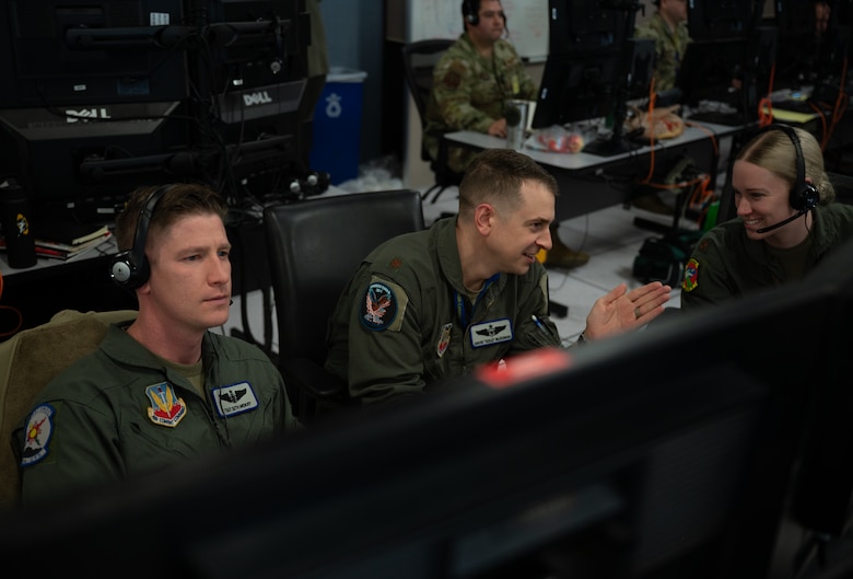 uniformed USAF and RCAF members wearing headsets work on computers