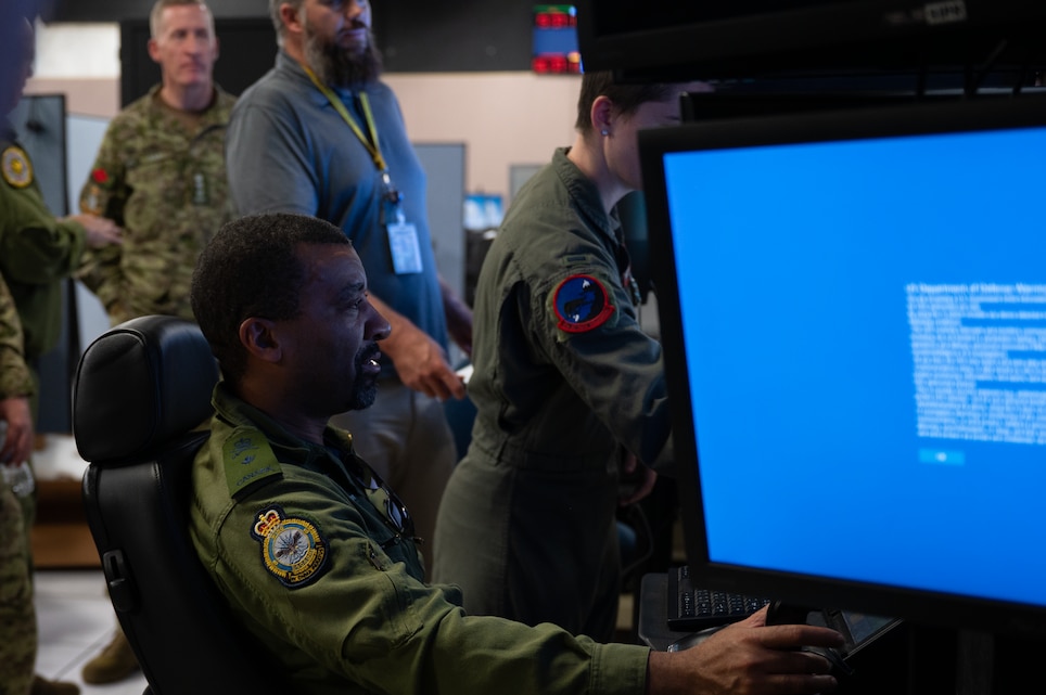 uniformed coalition and U.S. Airmen around a flight simulator