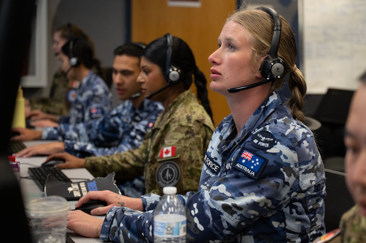 uniformed RAAF and RCAF members wearing headsets work on computers