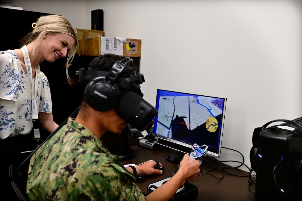 Allison Bayro, an intern with the Naval Research Lab observes a naval aviation candidate using a virtual reality (VR) testing station equipped with Assessing Spatial Abilities in Naval Aviation (ASANA) in the Naval Aerospace Medical Institute's (NAMI) behavioral research lab, Aug. 4. Users of the system must navigate immersive scenarios with ever increasing levels of difficulty and are asked to answer questions designed to test a person's ability to multitask and think abstractly. ASANA uses eye tracking, bio metric, reaction time, and behavioral monitoring to collect data in order to pair with a user's aptitude testing data to help determine their viability as an aviation officer candidate. With five detachments, 12 training centers, and facilities in over 60 locations across the United States, NMOTC provides high impact individual medical training for the Navy, other U.S. armed forces, and allied nations around the globe. (U.S. Navy photo by Mass Communication Specialist 1st Class Russell Lindsey SW/AW)