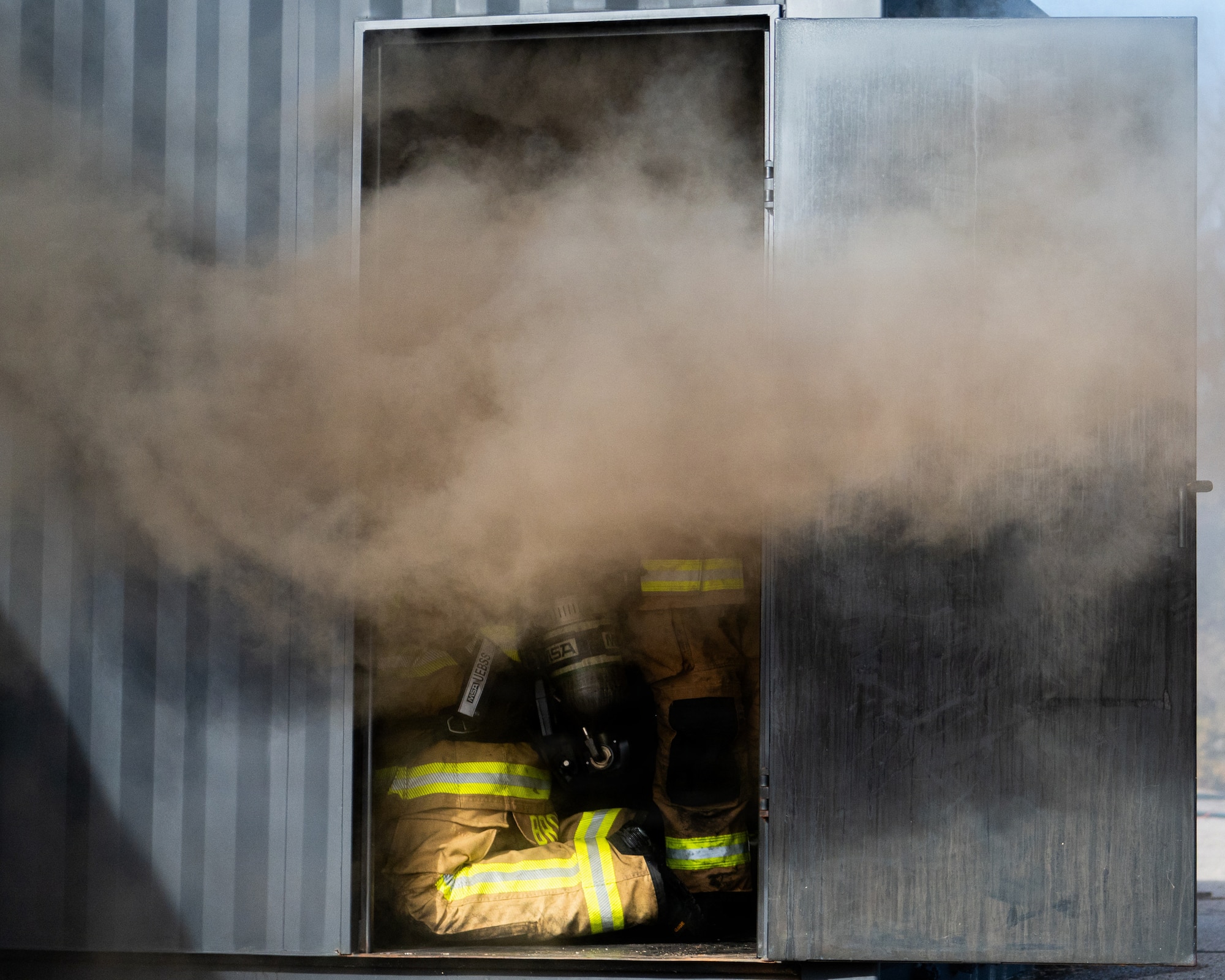 The lower half of a firefighter is visible kneeling in a doorway billowing with dark smoke.