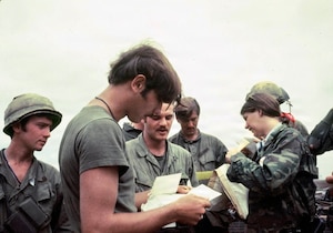 A woman wearing a military camouflage jacket distributes mail to soldiers in various states of dress in this Vietnam War-era photo.