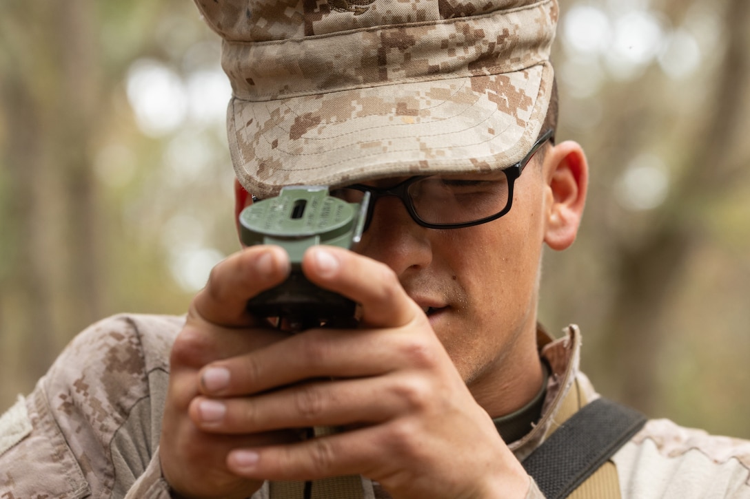 A close-up of a Marine Corps recruit using a lensatic compass during the day.
