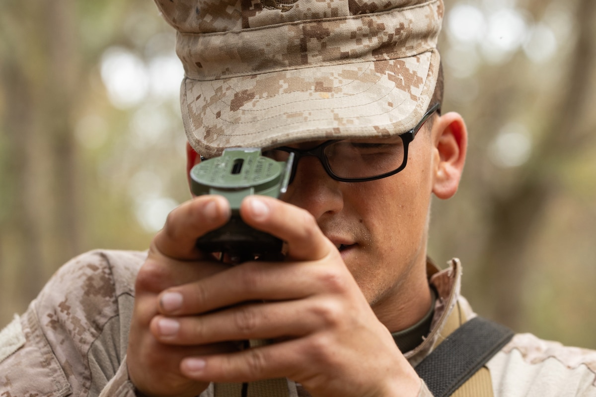 A close-up of a Marine Corps recruit using a lensatic compass during the day.