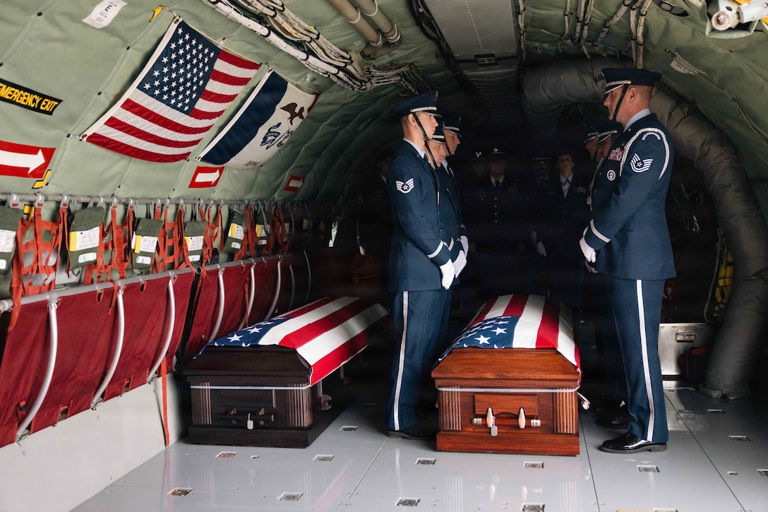 Airmen in ceremonial dress stand in formation near two caskets covered with American flags.