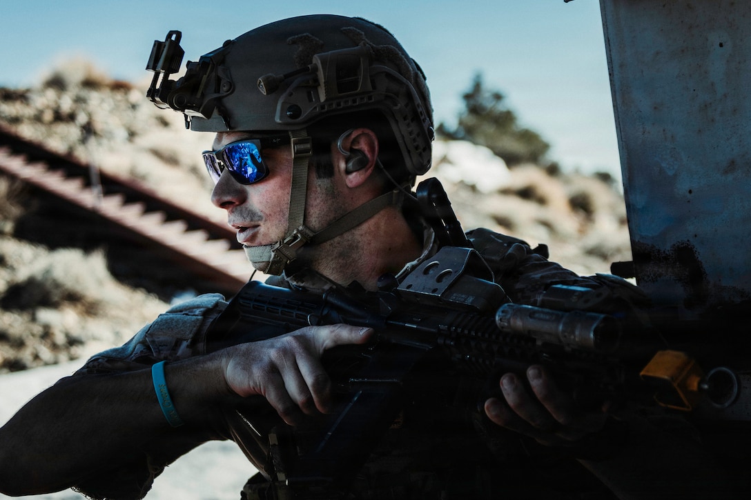 A close-up of a sailor in tactical gear holding a weapon on the dark corner of a building.