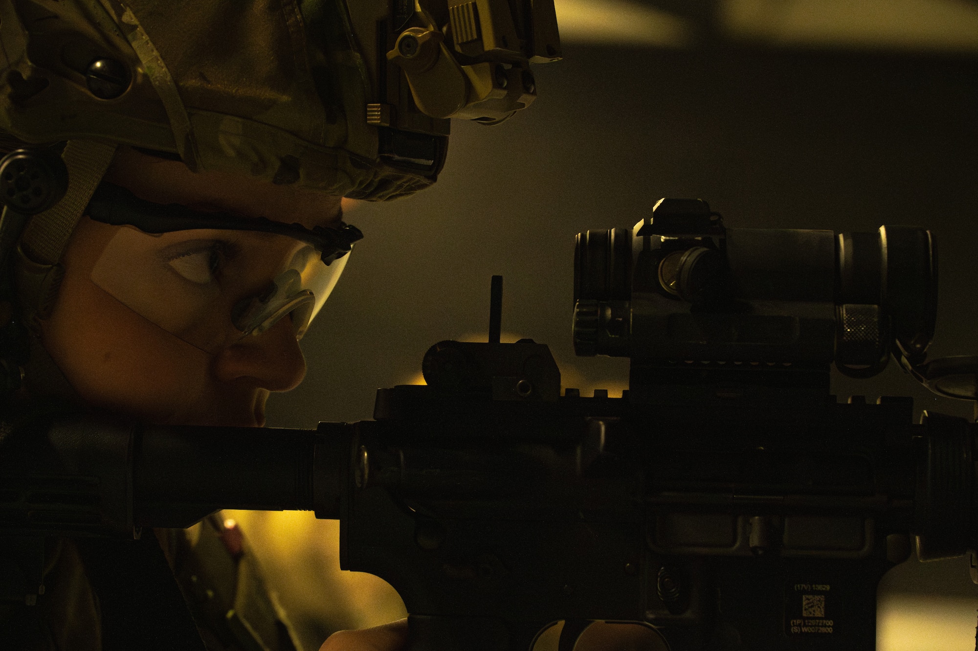 Close up of an Airman in tactical gear looking through an optical mounted on a weapon