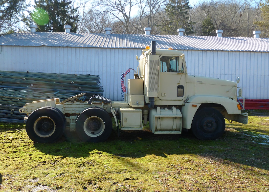 A military cargo truck painted tan sits outside in what looks like a back lot.