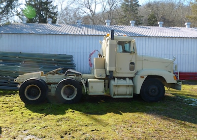 A military cargo truck painted tan sits outside in what looks like a back lot.