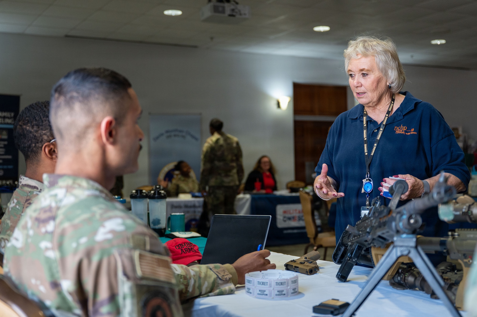 U.S. Air Force combat arms team members talk with community members about weapon safety at Davis-Monthan Air Force Base, Arizona, Dec. 23, 2025. The Community Action Team and UNITE program hosted a “Connect 4 Wellness” fair, bringing Airmen together with free food, games, and wellness activities to celebrate the holidays. (U.S. Air Force photo by Senior Airman Jasmyne Bridgers-Matos)