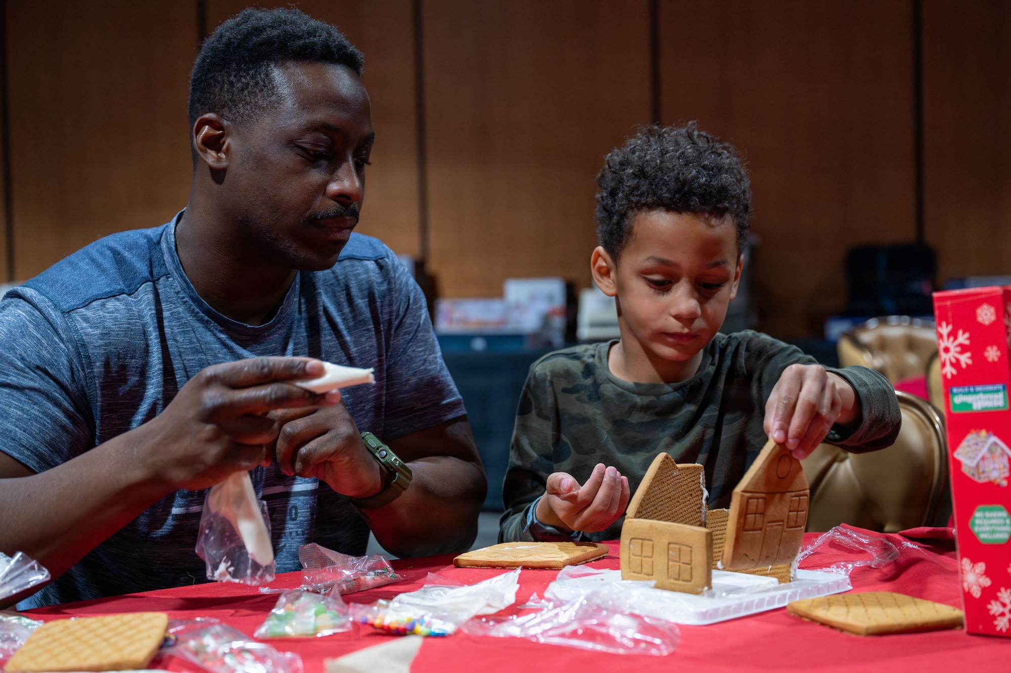 A U.S. Airman builds a gingerbread house with his son during the “Connect 4 Wellness” fair at Davis-Monthan Air Force Base, Arizona, Dec. 23, 2025. The Community Action Team and UNITE program hosted the fair to bring the Desert Lightning team together for free food, games, and wellness activities to celebrate the holidays. (U.S. Air Force photo by Senior Airman Jasmyne Bridgers-Matos)