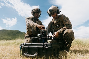 Two Marines in an open field kneel by a military drone.