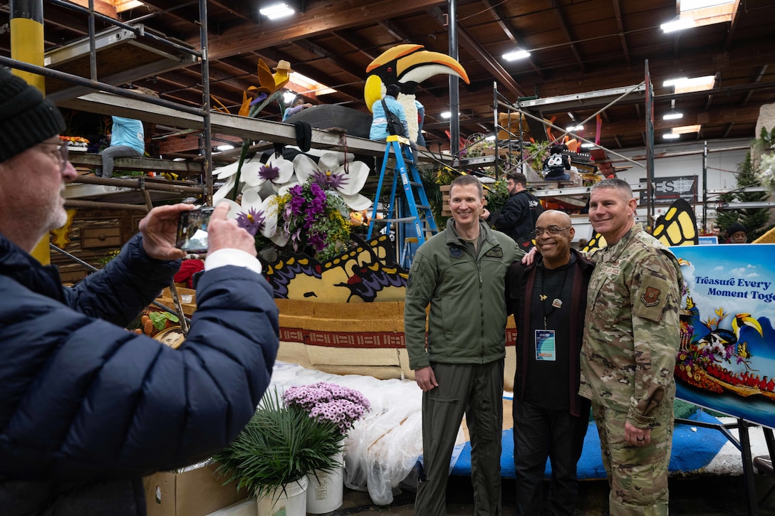 Three people smile next to parade floats as someone takes their photo.