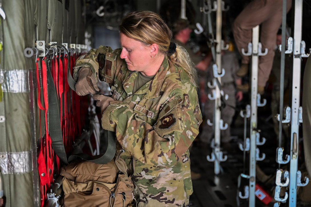 An airman works on adjustable wall fixtures as fellow service members work in the background.