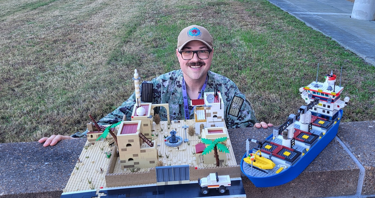 Petty Officer 1st Class Eric Anderson, an Information Warfare Training Command Virginia Beach instructor, displays the mock Lego insurgent compound and merchant shipping vessel he built for use in various intelligence courses at Naval Air Station Oceana’s Dam Neck Annex in Virginia Beach, Virginia, Nov. 19, 2025. The complex designs and creative process didn’t just produce a training tool – it sparked new ways to enhance learning for Navy and joint service information warfare professionals. (U.S. Navy photo by Lt. Isabel Shaw)