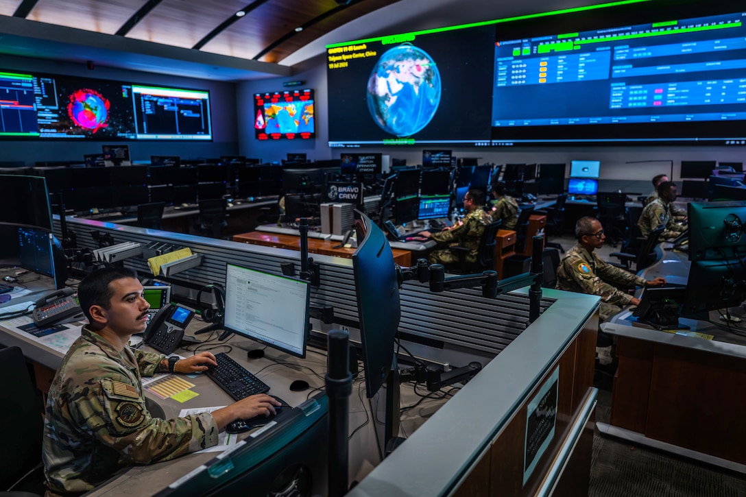 Guardians work on computers at workstations in a large room with screens showing data on the walls.