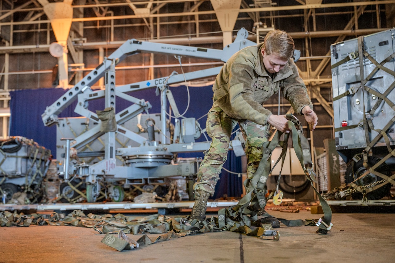 An airman unfurls cargo straps inside a building.