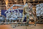 An airman unfurls cargo straps inside a building.