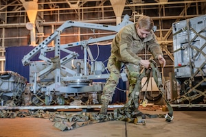 An airman unfurls cargo straps inside a building.