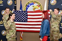 U.S. Army Maj. Lauren Hall administers the Oath of Enlistment during a ceremony for Sophie Marie Stewart on Jan. 29, 2025, while recruiters, Sgt. 1st Class Chuck Vandell (left) and Staff Sgt. Chance Schutter (right), hold the U.S. flag at U.S. Army 2nd Recruiting Brigade, Redstone Arsenal, AL. Stewart enlisted as a 68T Animal Care Specialist, taking the first steps towards fulfilling her dream of a career in the medical field.