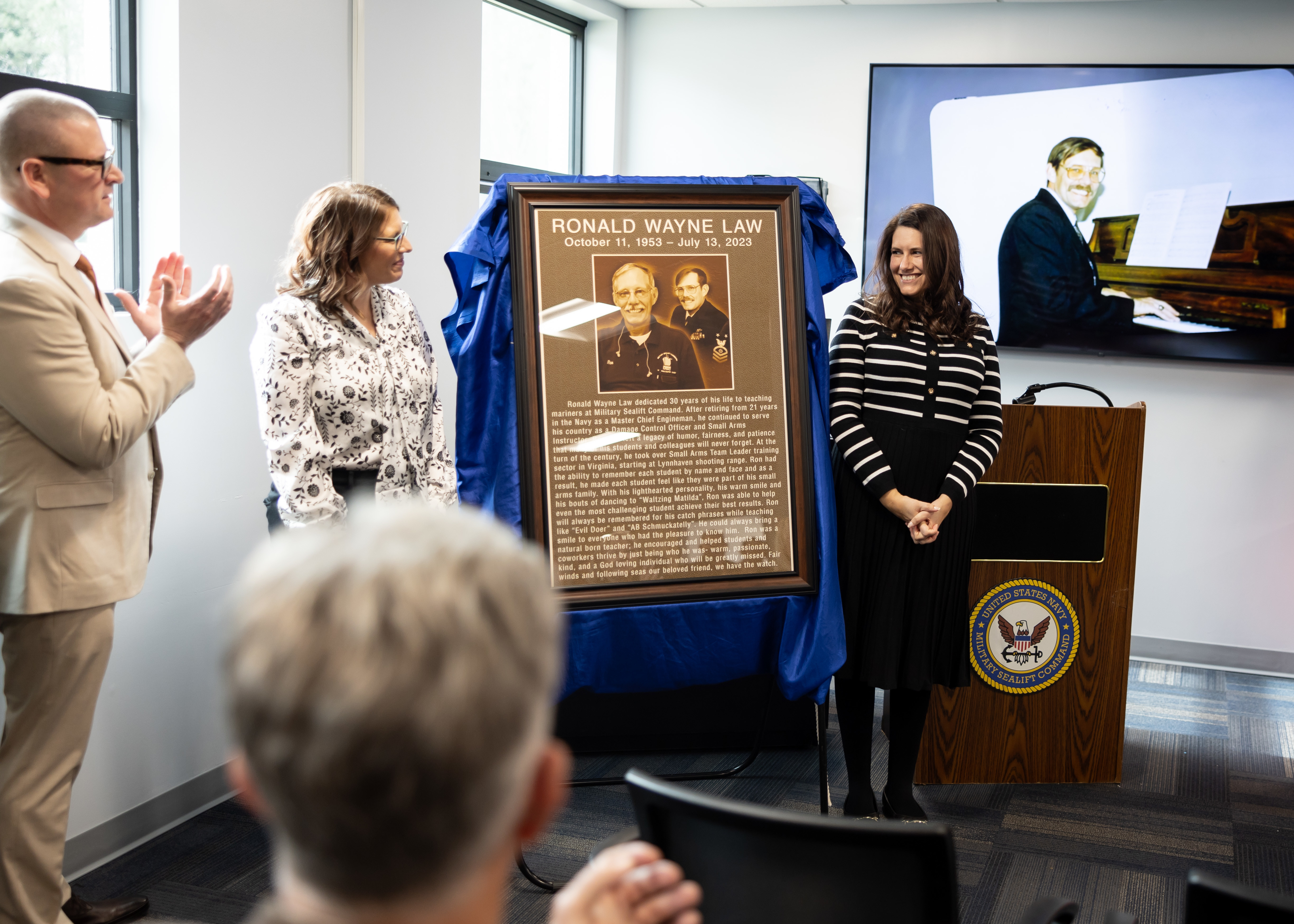 The plaque dedicated to Ronald “Ron” Law is unveiled during the Ron Law Small Arms Marksmanship Training Center (SAMTC) building dedication, held in the building Jan. 23, 2025. The building has been named after Ronald “Ron” Law, who dedicated 30 years of his life to Military Sealift Command as a Damage Control Officer and Small Arms Instructor.