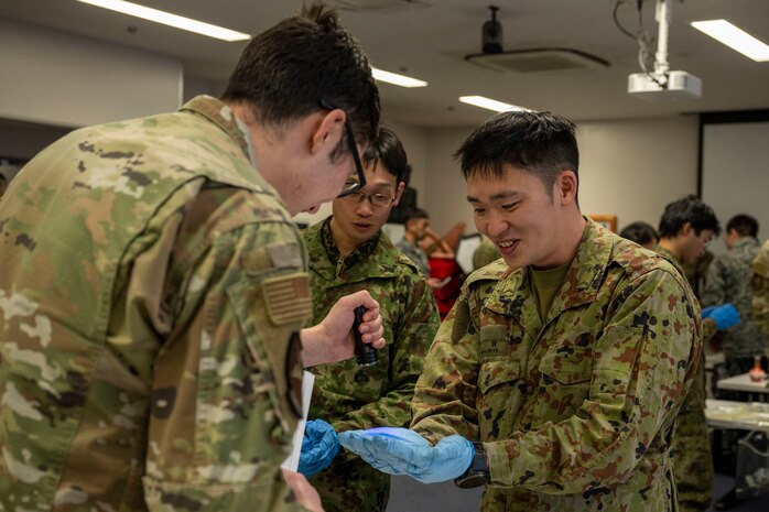 U.S. Air Force Airman 1st Class Tristian Worley, left, 35th Civil Engineering Squadron emergency manager, examines a participant’s gloves for residue during a bilateral chemical, biological, radiological and nuclear (CBRN) training.