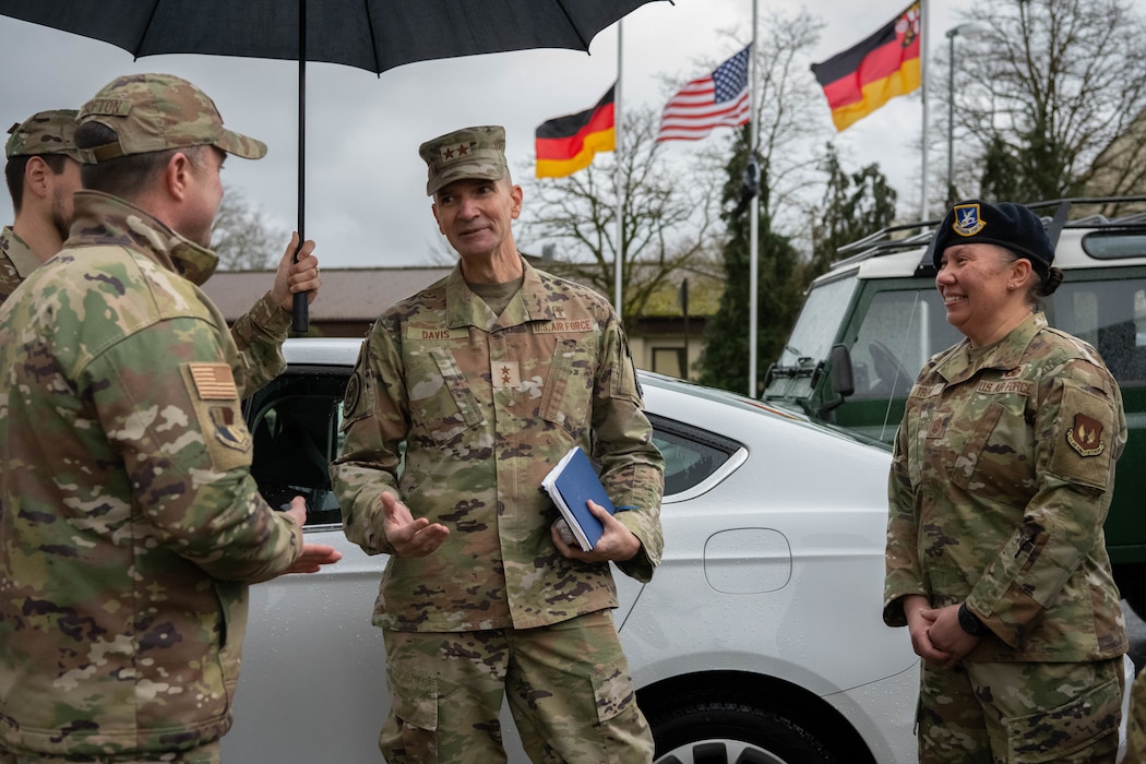 A U.S. Air Force major general speaks to a colonel and a chief master sergeant in front of a white car.